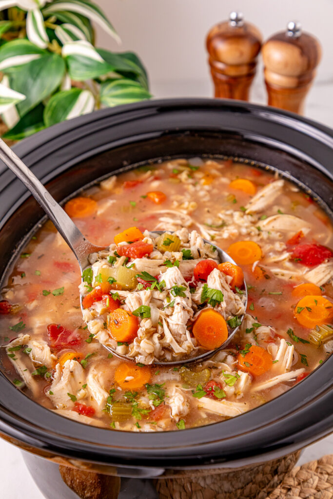 Crockpot chicken and barley soup in crockpot scooped up with a ladle.