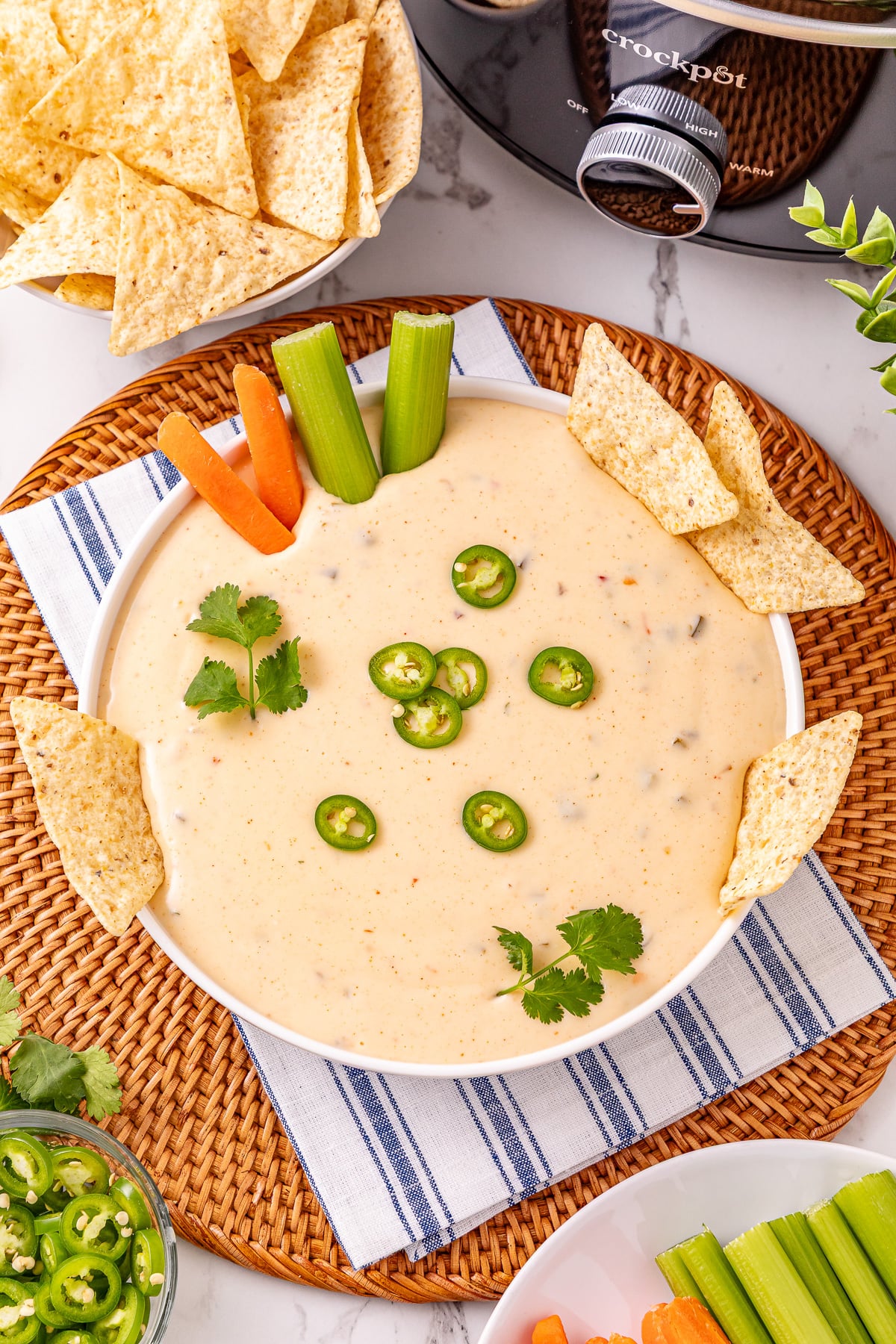 Crockpot queso blanco in white bowl with sliced carrots and celery on the side.