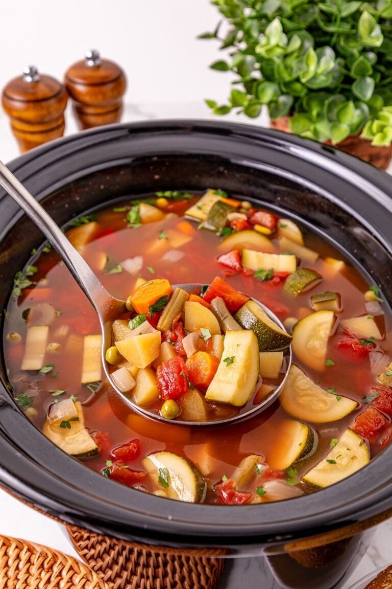Crockpot vegetable soup in slow cooker scooped up with a spoon.