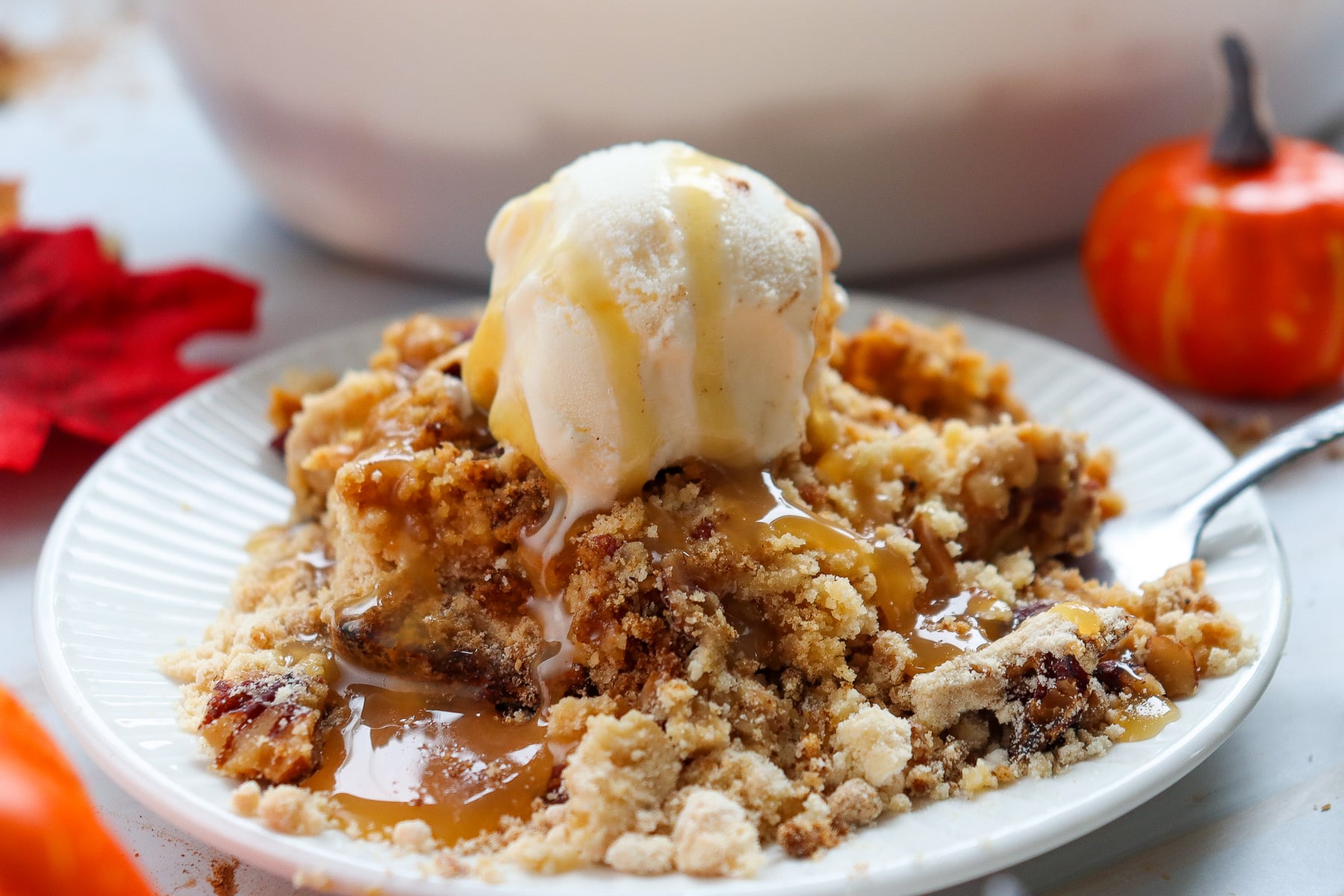 Ice cream-topped pumpkin cream cheese dump cake with caramel sauce served on a white plate.