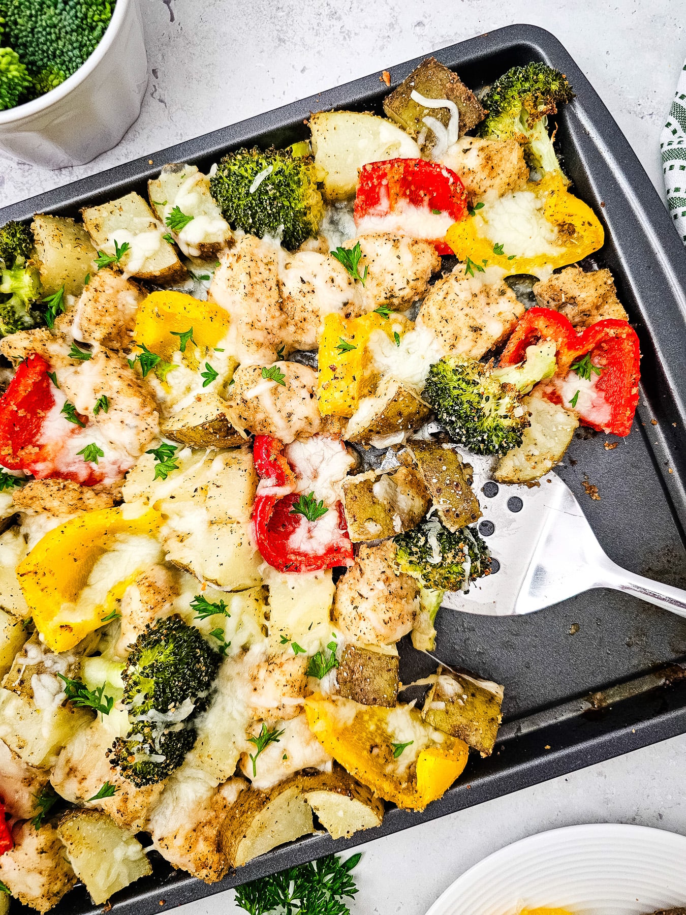 Sheet pan mozzarella chicken on baking sheet with serving spoon.