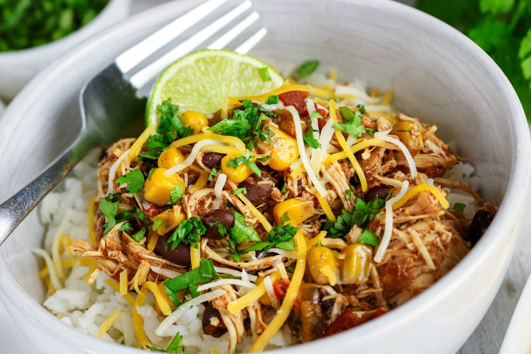 Close up image of crockpot southwest chicken in a bowl with rice and shredded cheddar cheese.