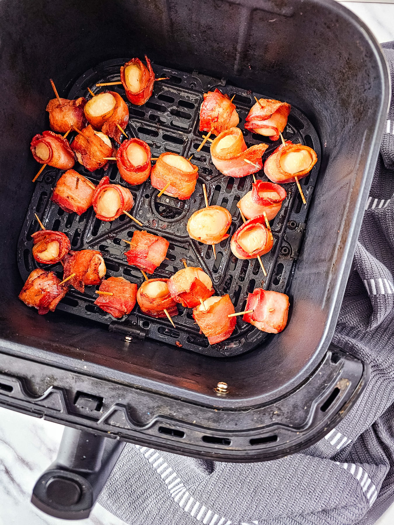 Cooked bacon-wrapped water chestnuts in bottom of the air fryer basket.