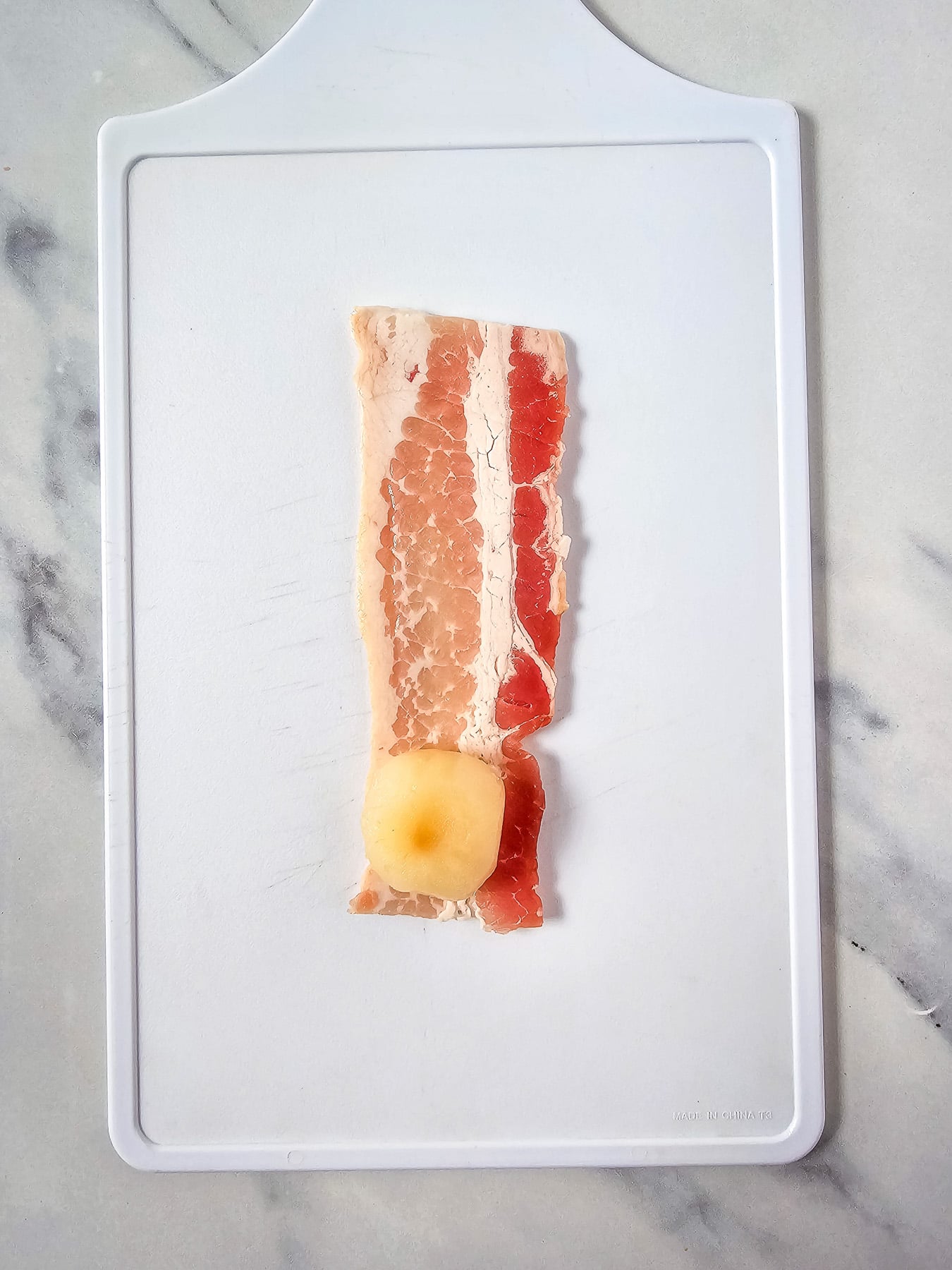 Water chestnut is placed at the bottom of the cut piece of bacon and ready to be rolled.