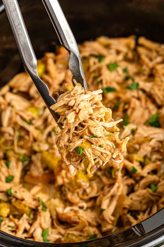 Crockpot Mississippi chicken held in tongs over slow cooker of chicken for a football party.