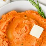 Mashed sweet potatoes in a bowl with a pat of butter.