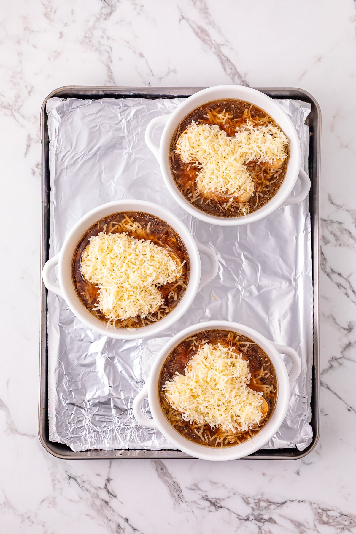 Gruyere and Parmesan cheeses are sprinkled on top of the baguettes in soup bowl.