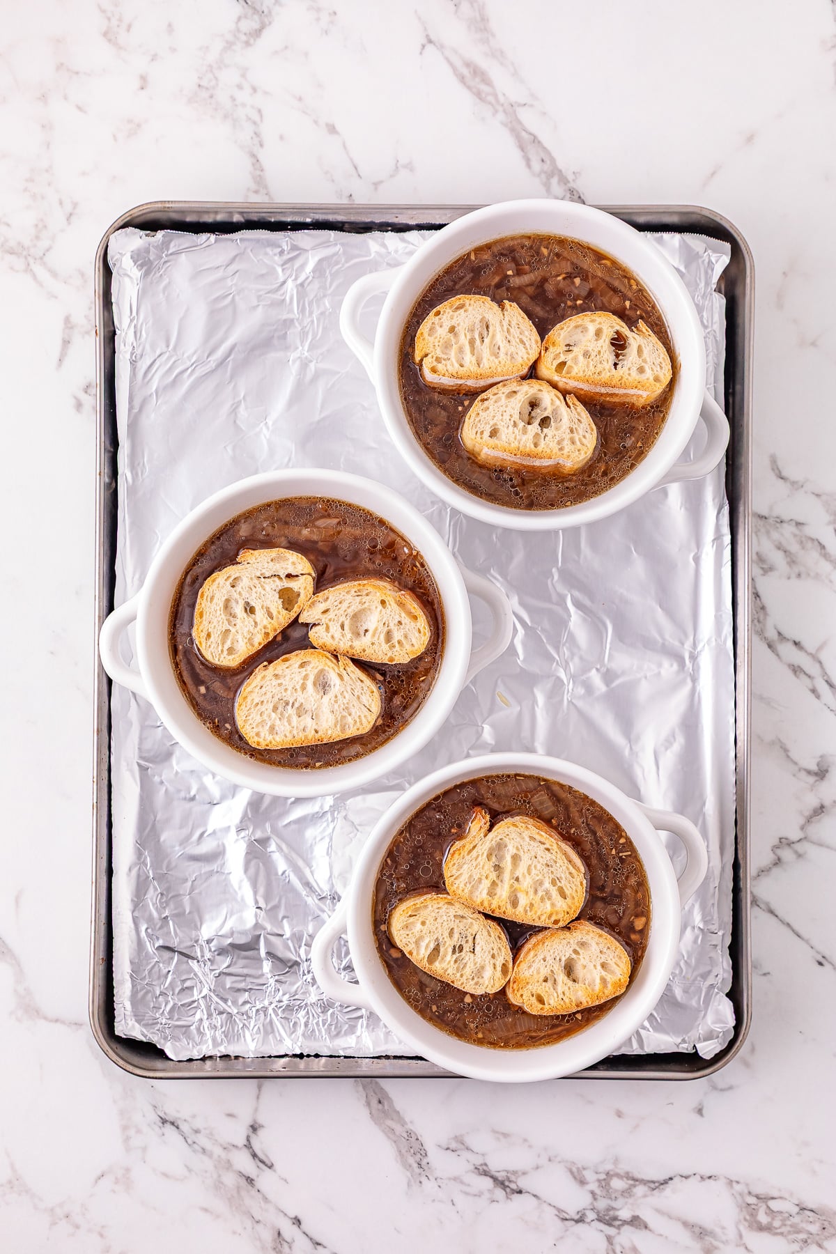 Toasted baguettes are placed in the soup bowls.
