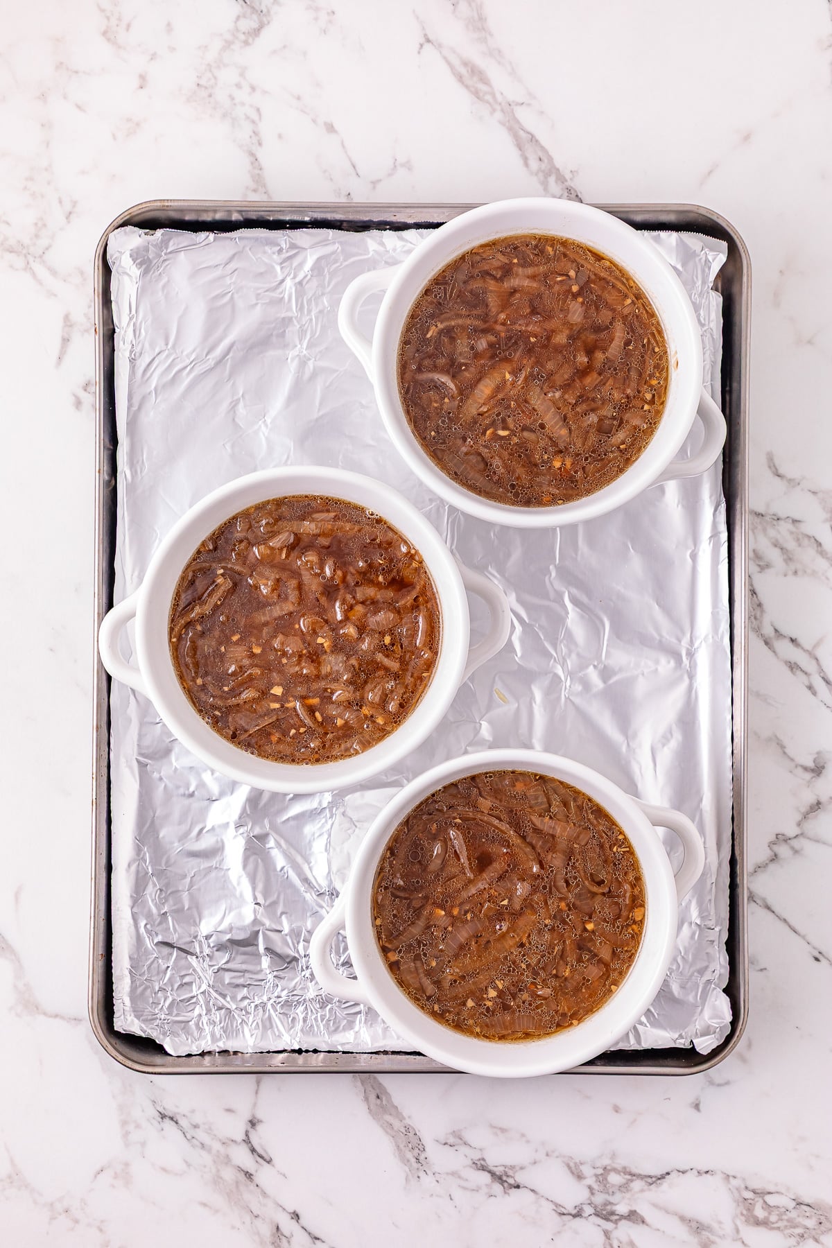 Soup is ladled into French onion soup bowls and placed on foil-lined baking sheet.