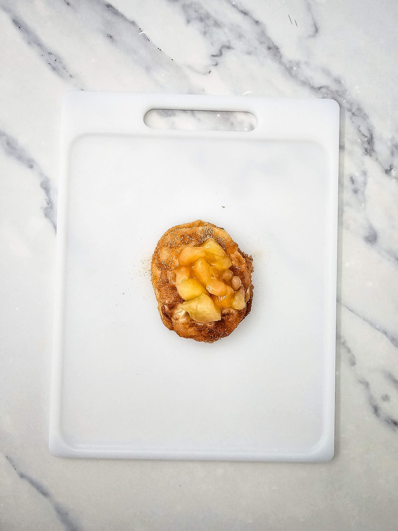Coated biscuits are placed on cutting board, then topped with apple pie filling.