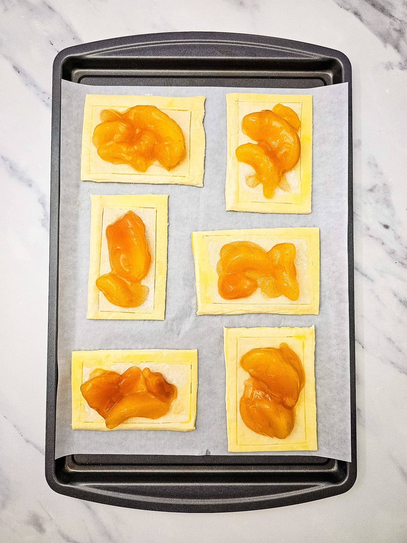 Apple pie filling in the middle of puff pastry on baking sheet.