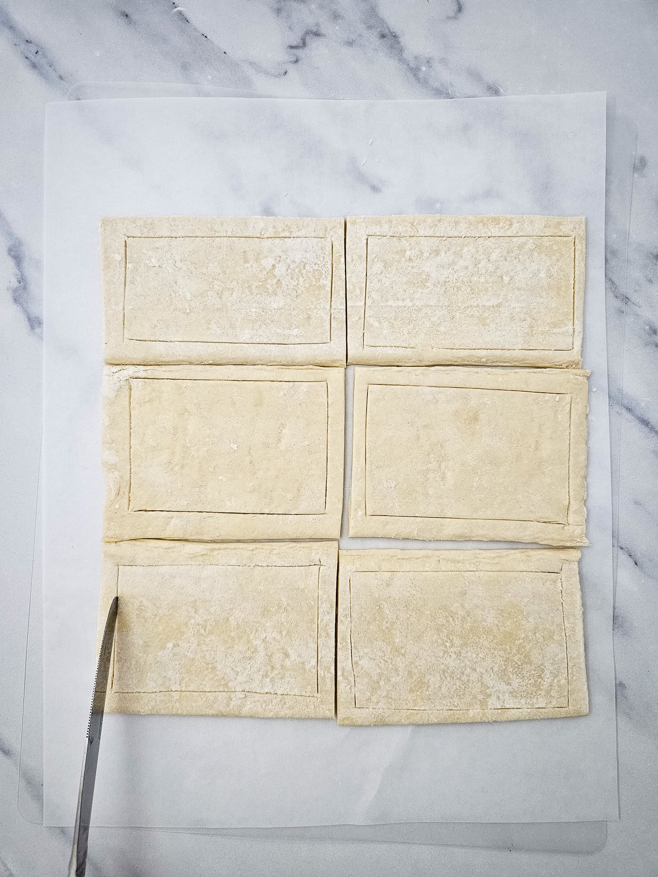 Unfolded puff pastry is cut into squares on cutting board.