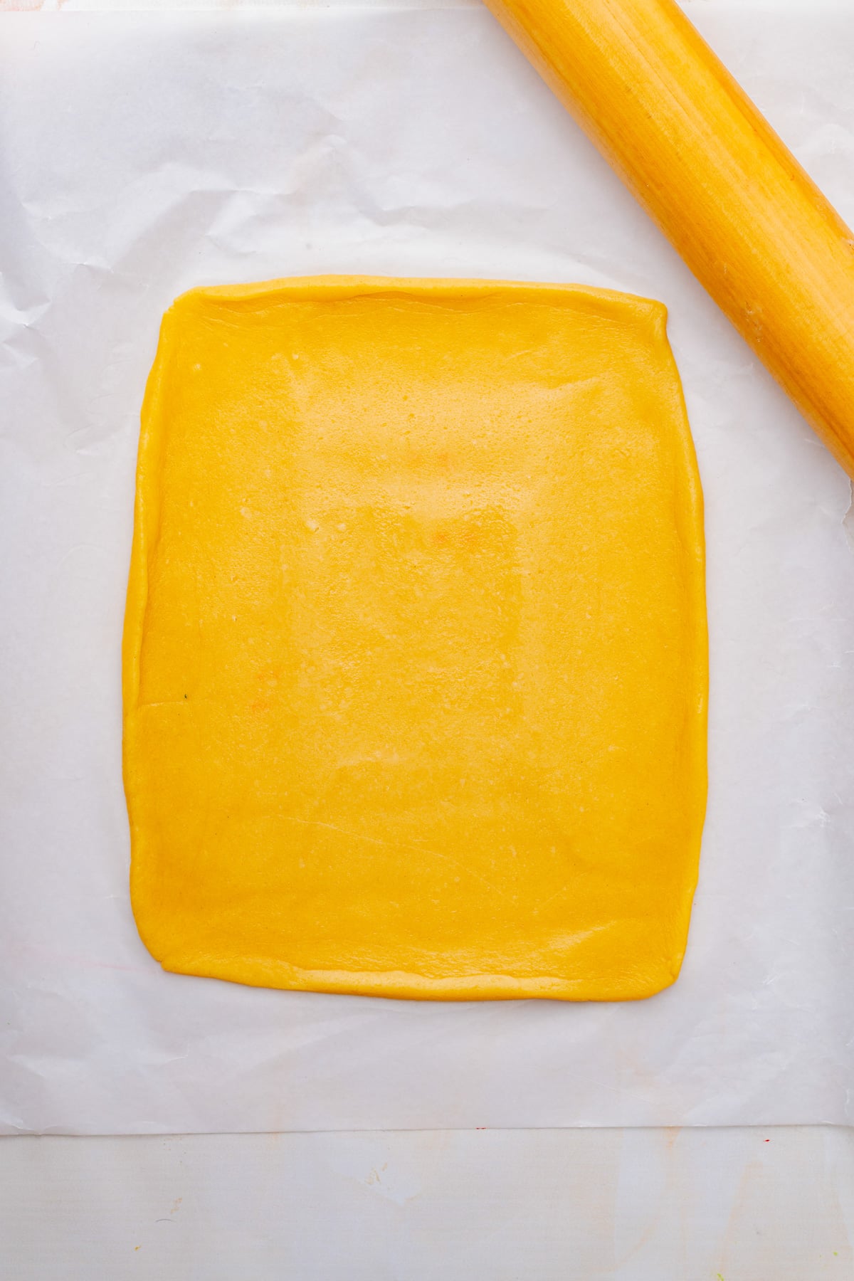 White cookie dough is rolled into a rectangle on parchment paper.