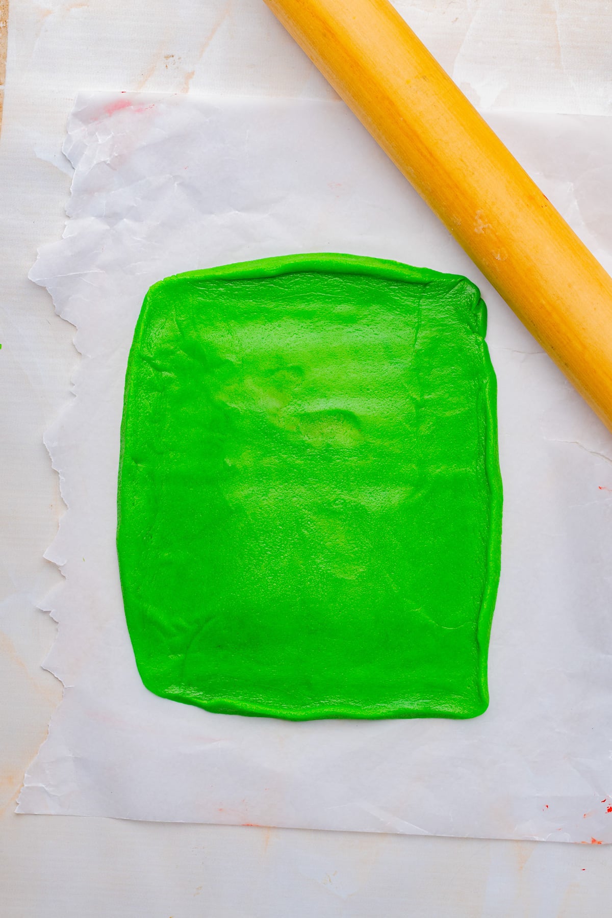 Green cookie dough is rolled into a rectangle on parchment paper.
