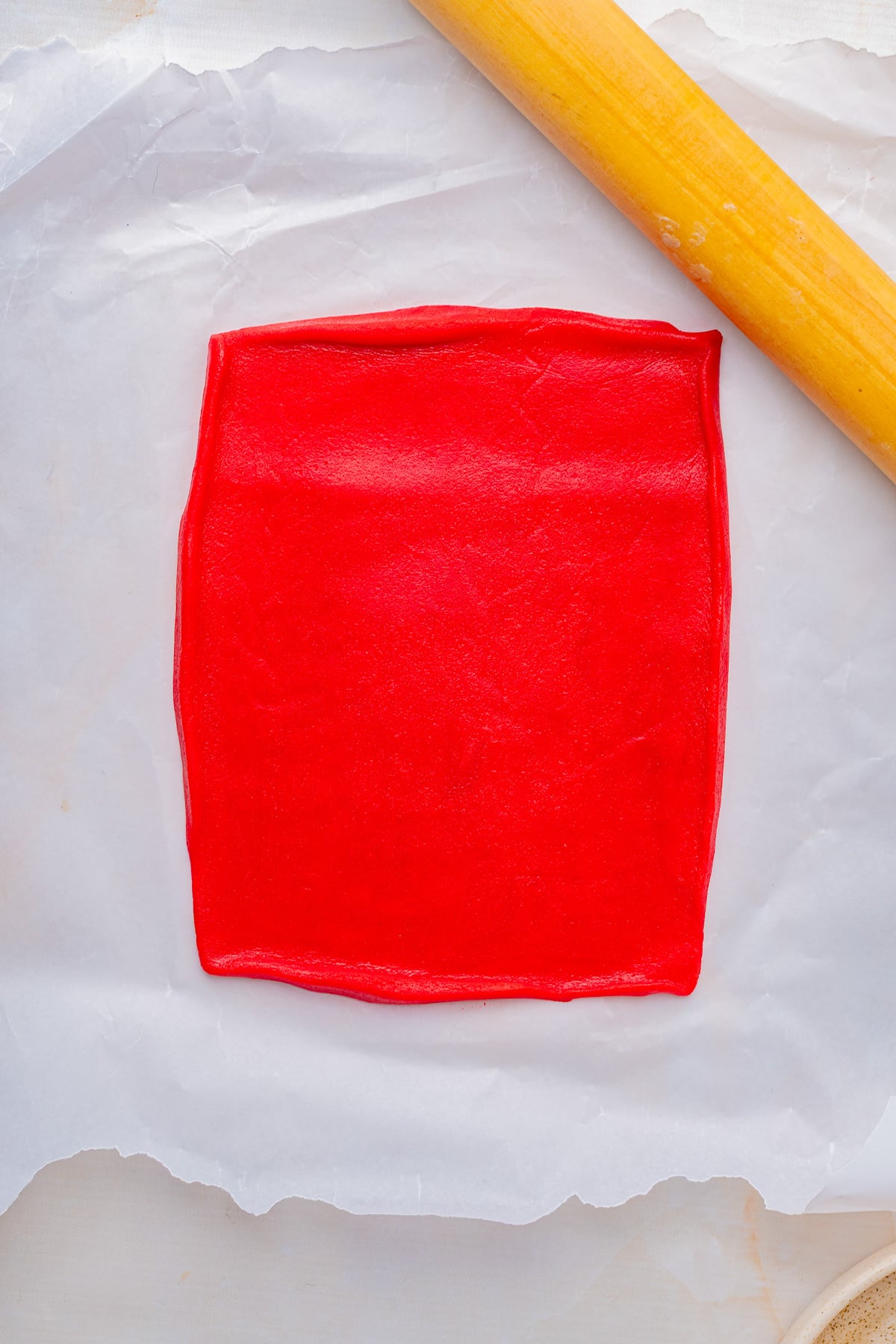 Red cookie dough rolled onto a rectangle on sheet.