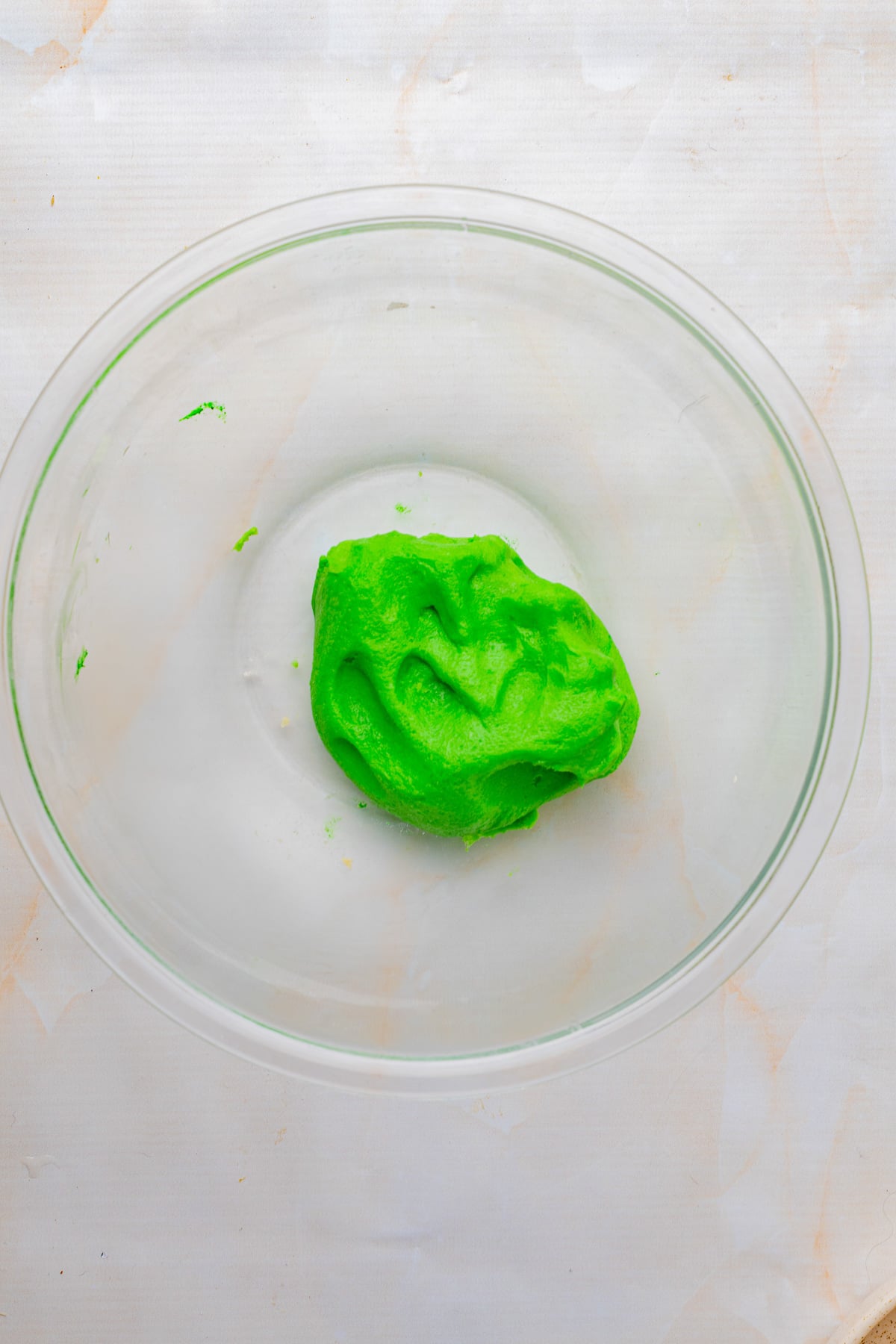 Green cookie dough ball in glass mixing bowl.