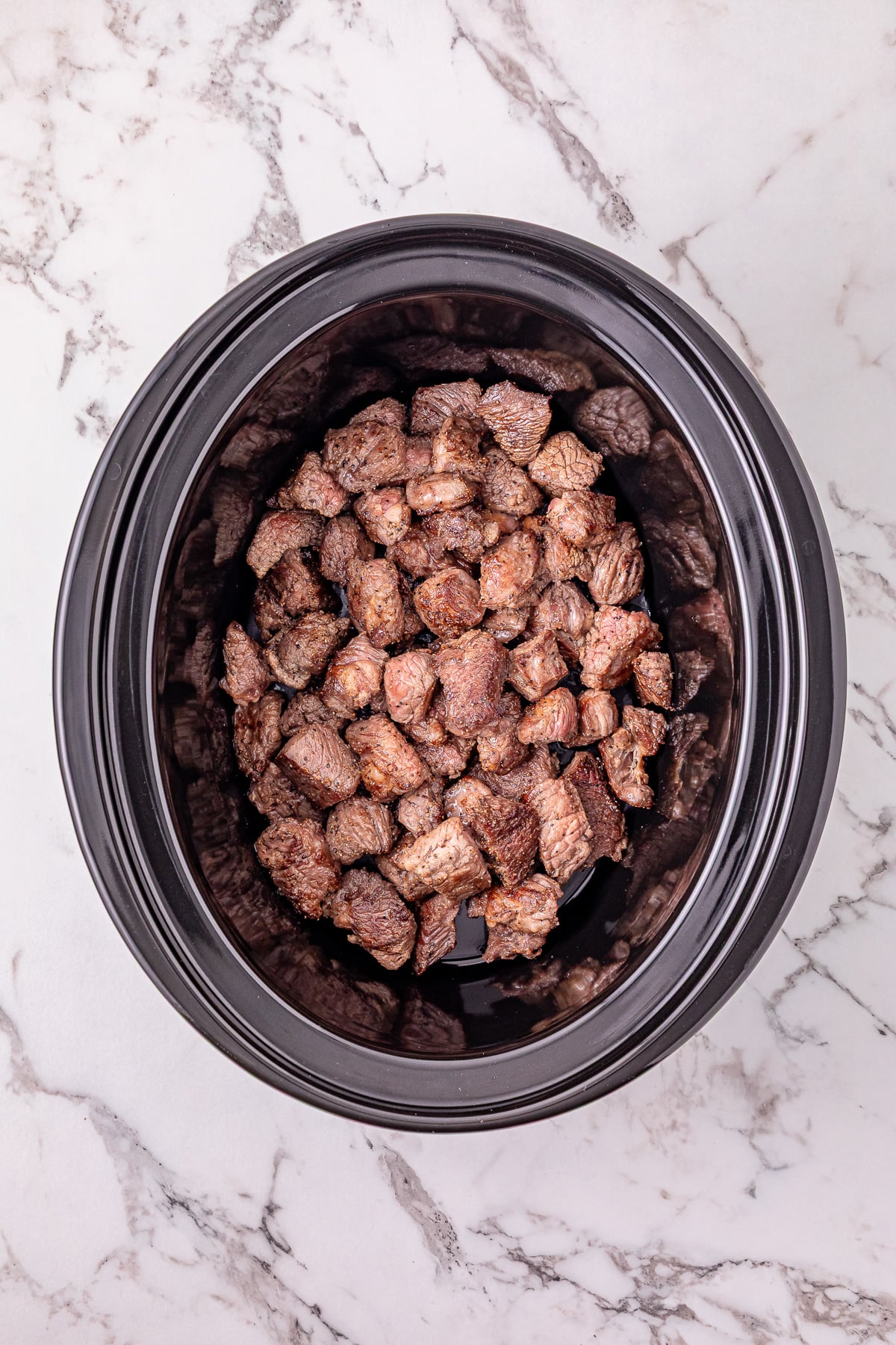 Seasoned browned beef is placed in the bottom of the crockpot.