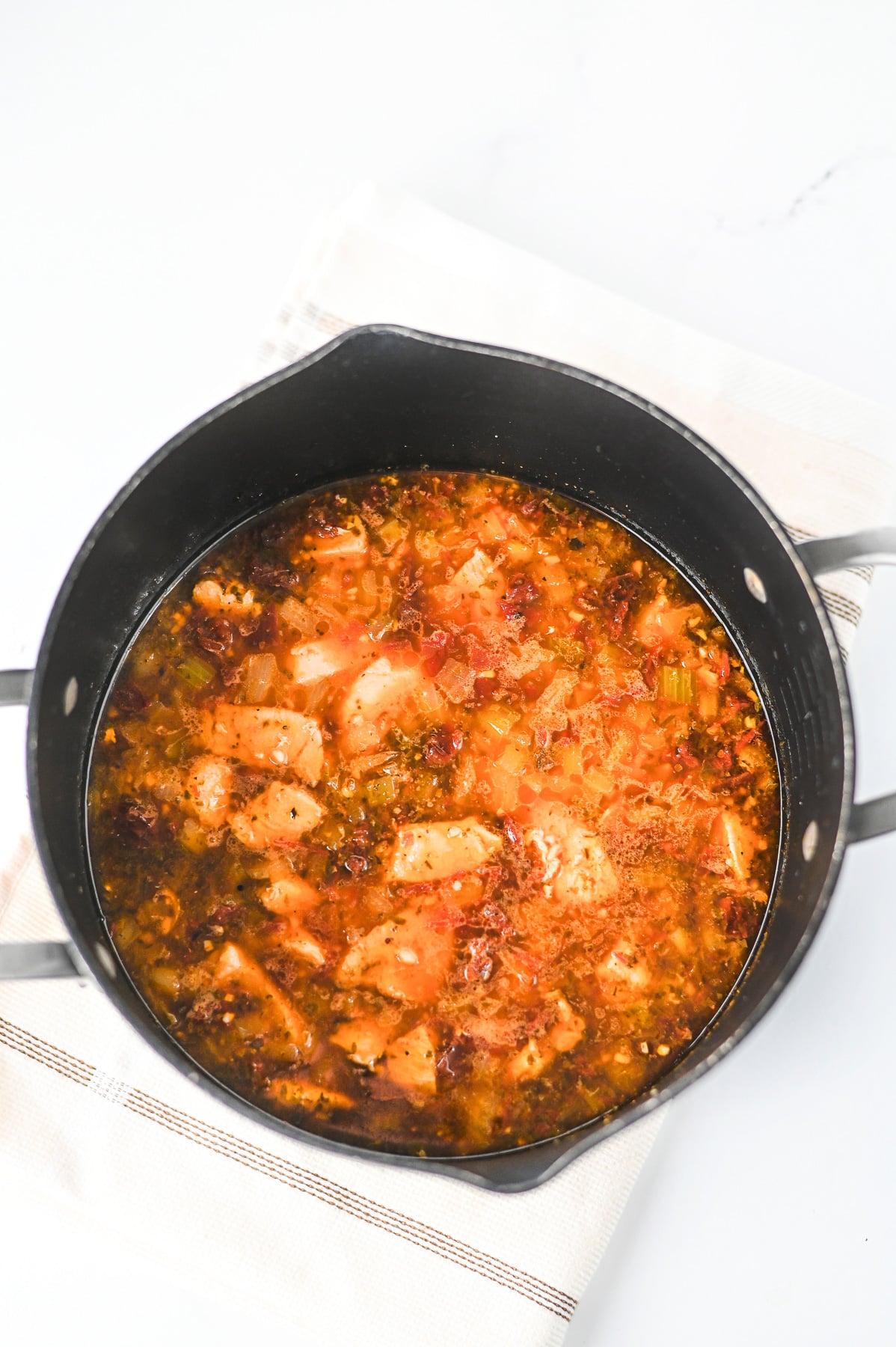 Sun-dried tomatoes, garlic, tomato paste, and pesto, then chicken broth are added to the pot with the chicken.