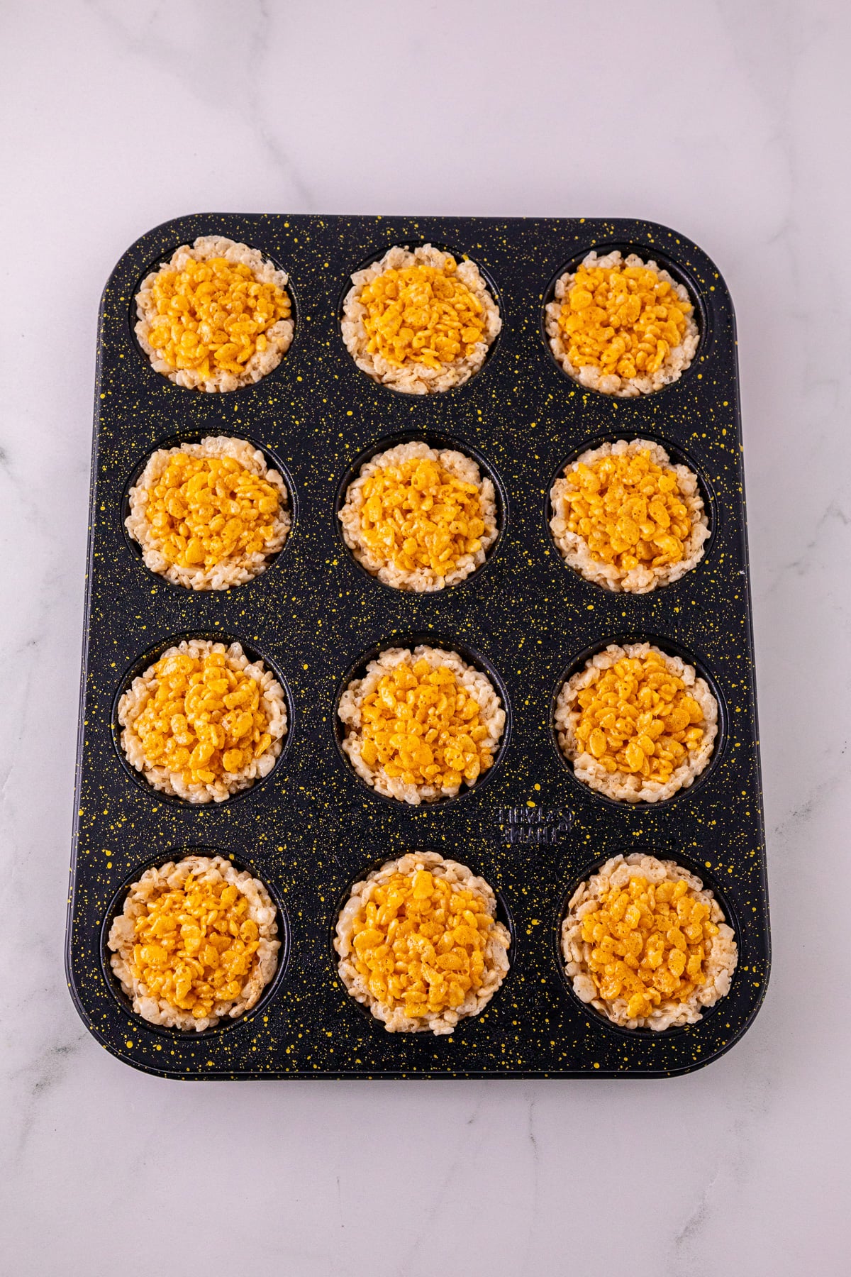 Orange Rice Krispie mixture is pressed into the centre of the other Rice Krispies in pan.