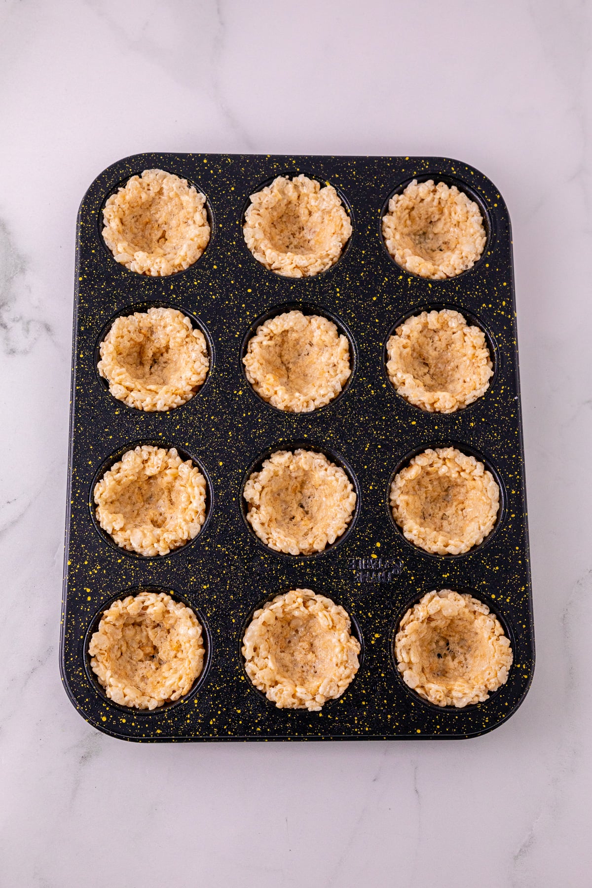 Rice Krispie mixture pressed into bottom of muffin tin with indent in middles.