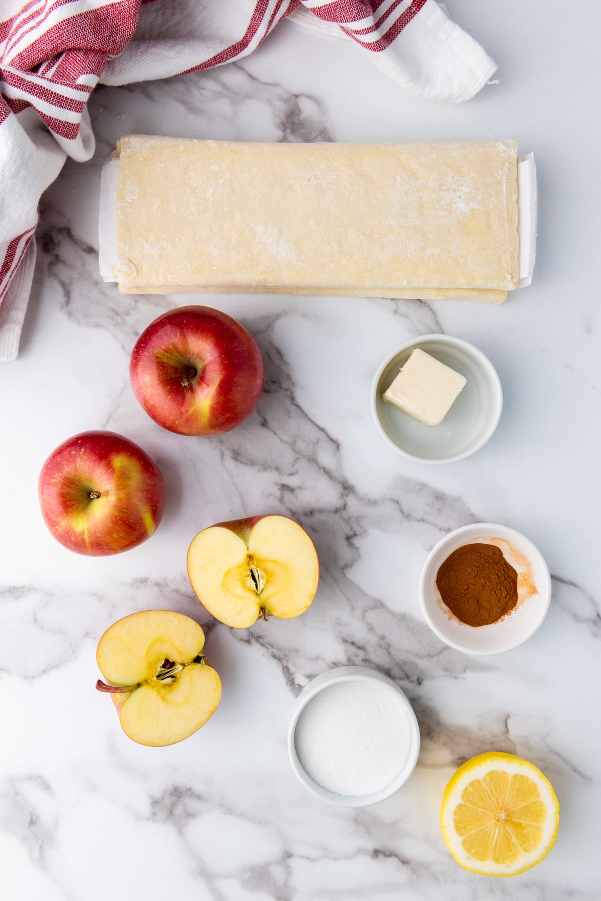 Ingredients for puff pastry apples laid out in small bowls on kitchen counter to prepare for the recipe.