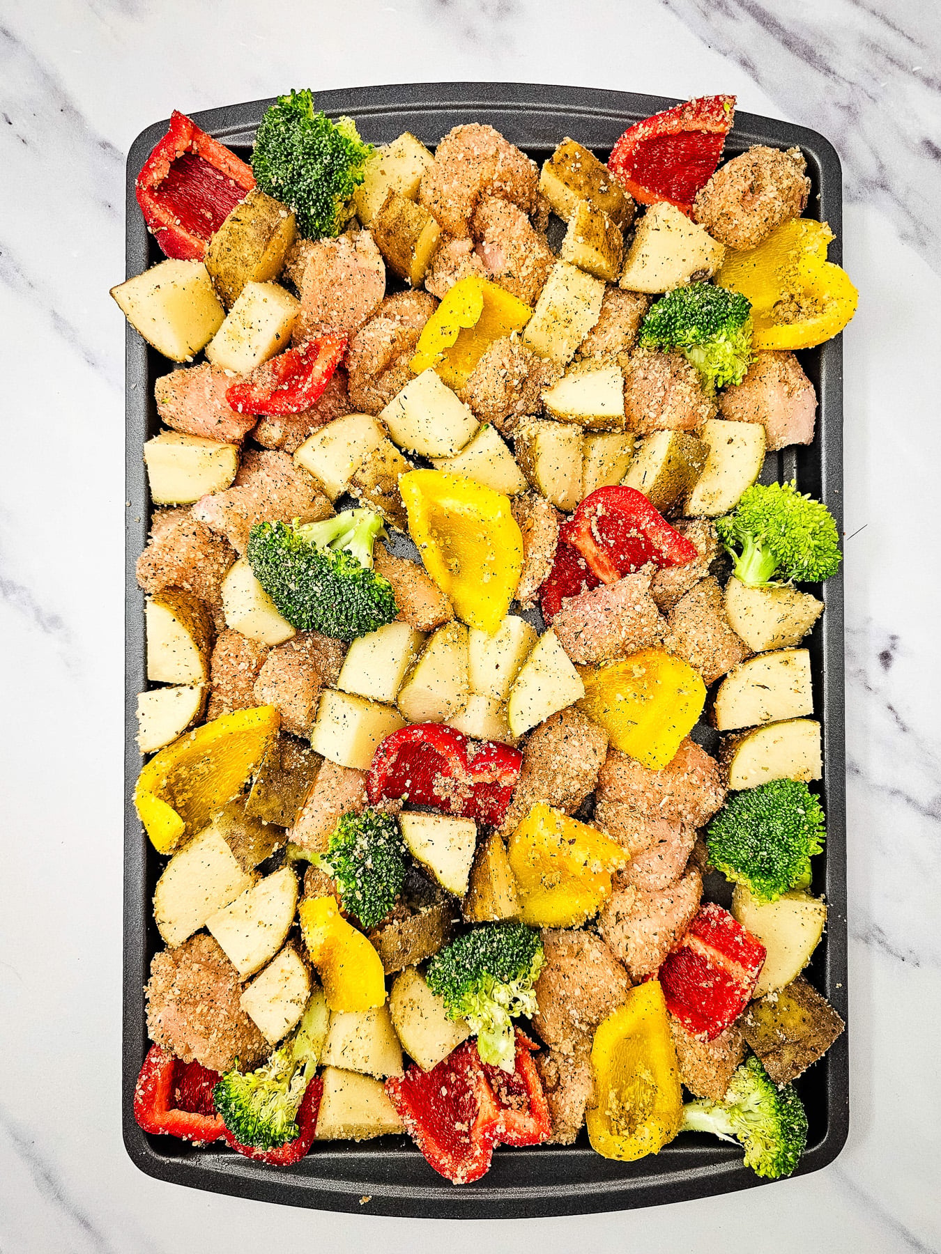 Chicken and vegetable mixture is spread out on sheet pan.