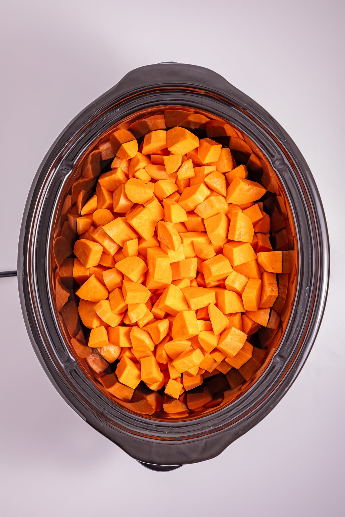 Cubed sweet potatoes in bottom of slow cooker.