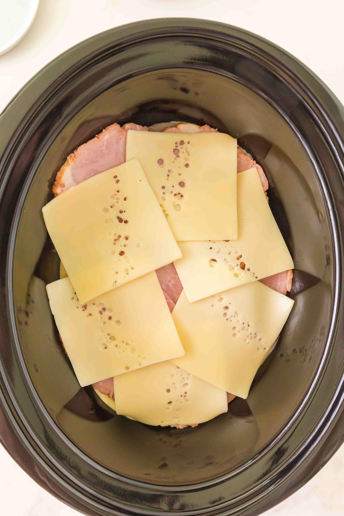 Layer of Swiss cheese is place on top of the ham in slow cooker.