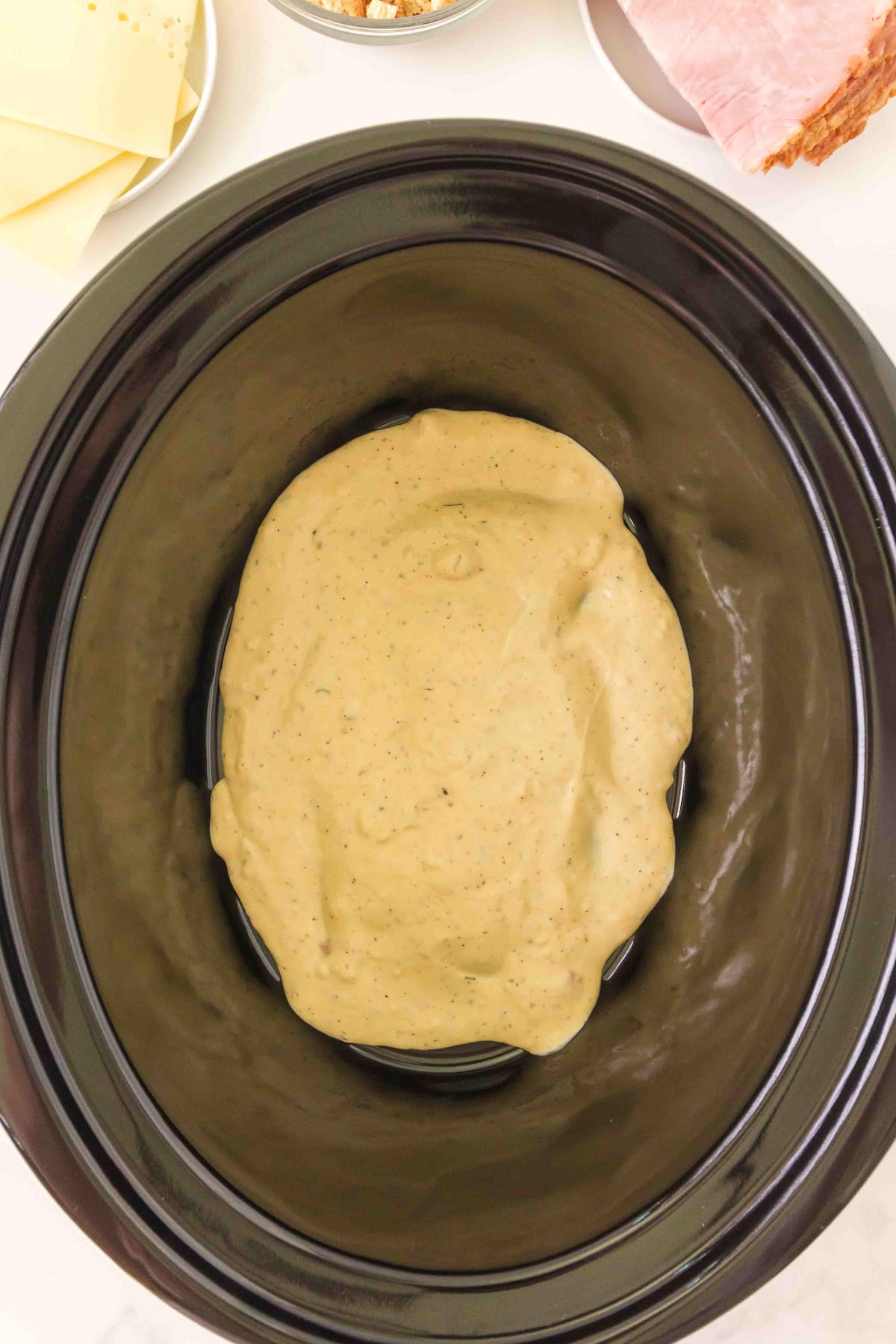 Half of the sauce is spread over the bottom of the slow cooker.