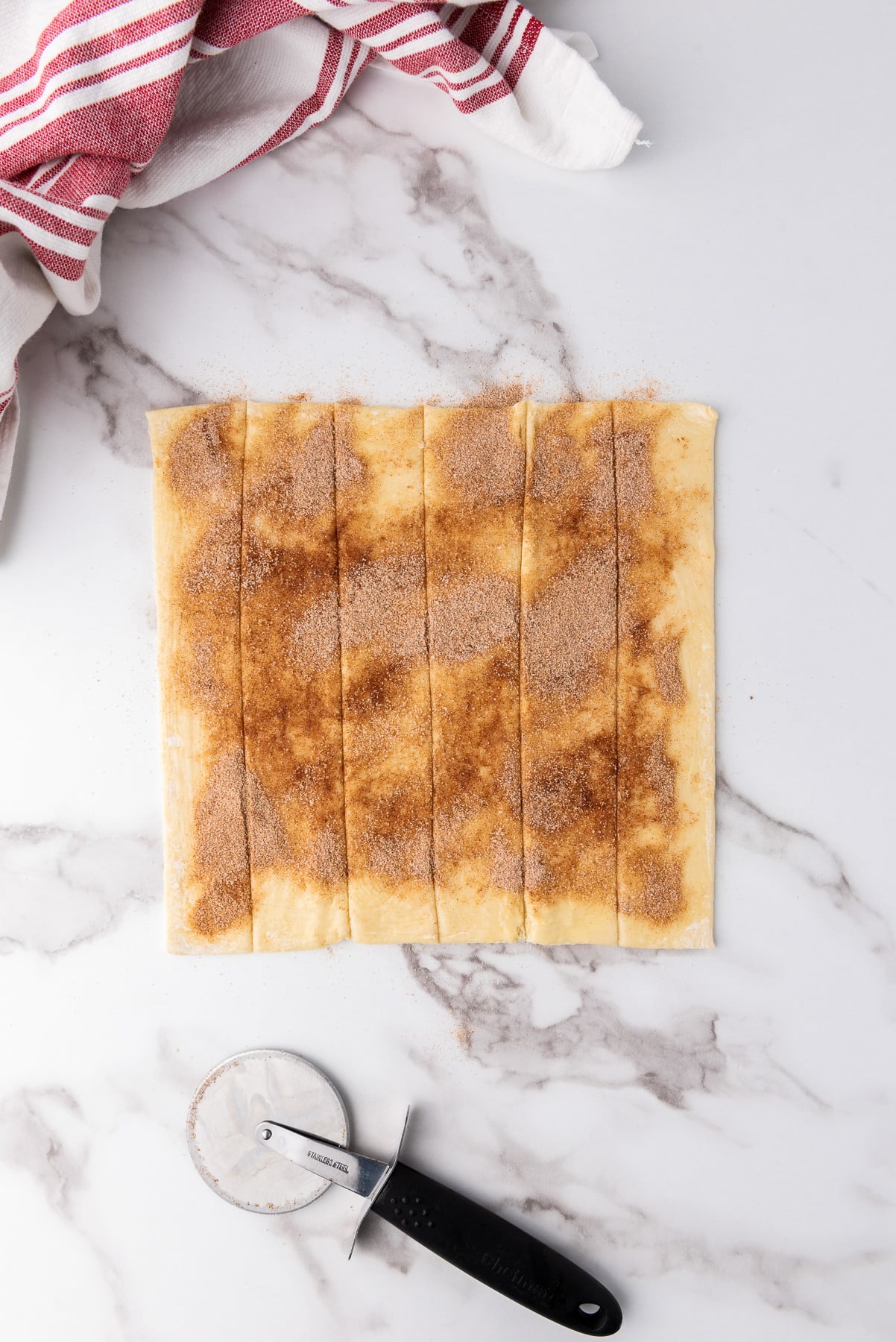 Cinnamon sugar is sprinkled on top of the buttered puff pastry then cut into strips with a pizza cutter.