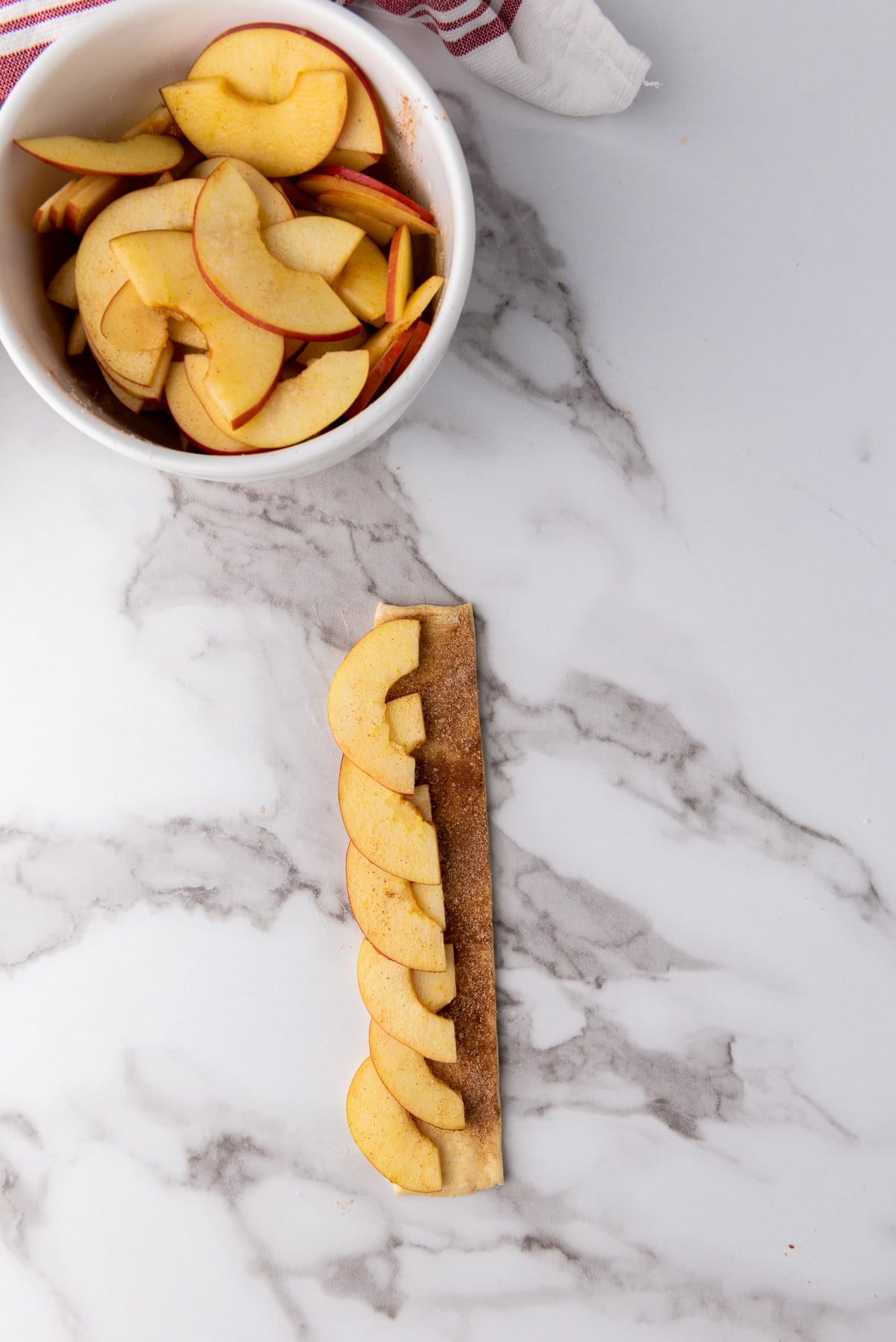 Sliced apples are placed in a single layer down the length of the cut strip of puff pastry.