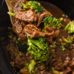 Finished beef and broccoli in wooden spoon held over slow cooker.
