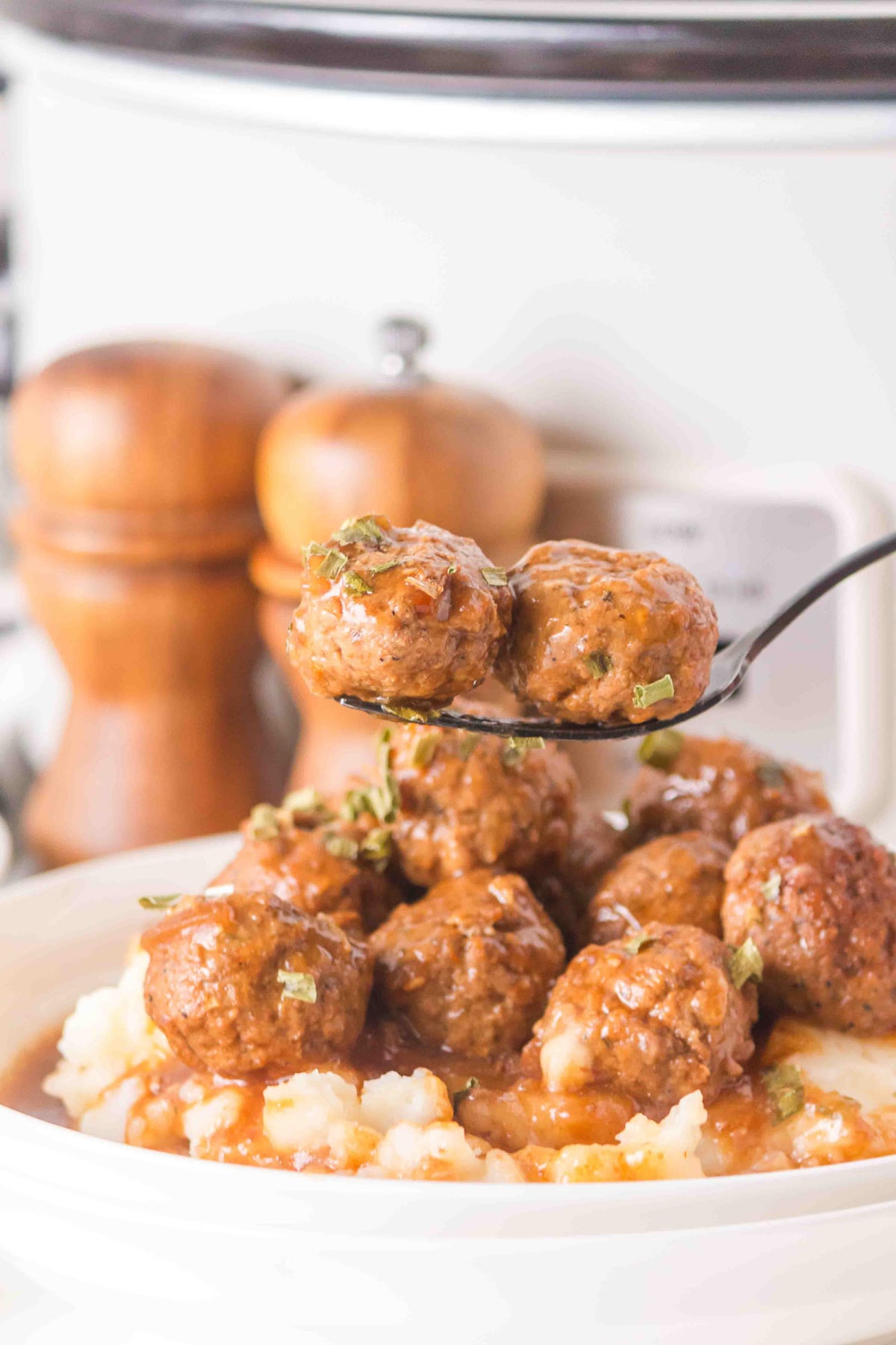 Two meatballs on a fork held over dish of salisbury meatballs for a family dinner.