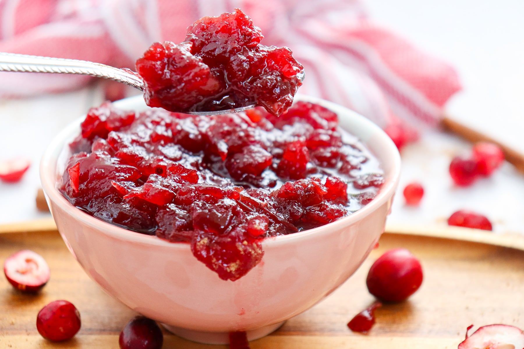 Cranberry sauce scooped up on spoon held over bowl of sauce.