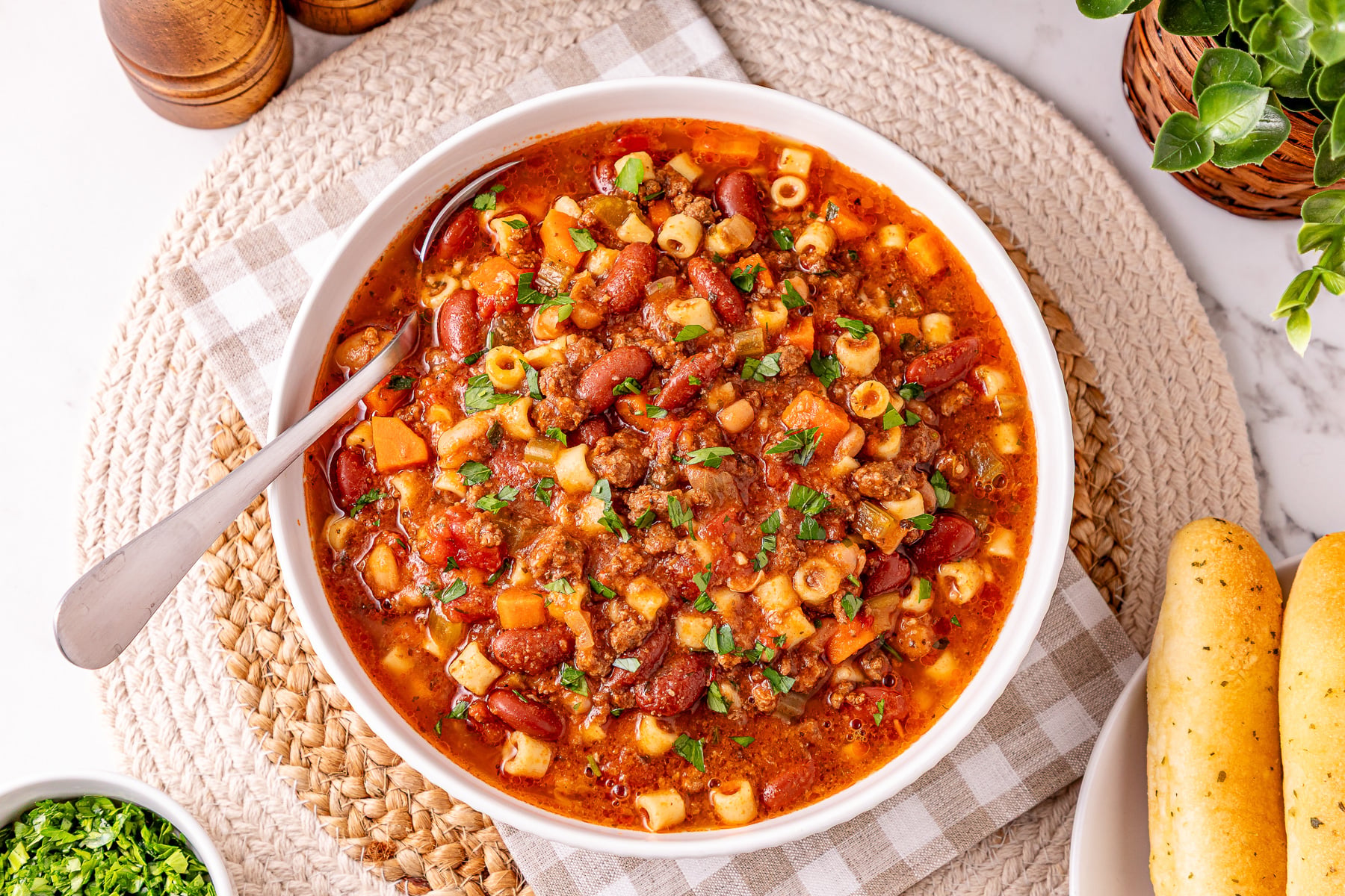 Pasta e fagioli soup in a white bowl with bread on the side.