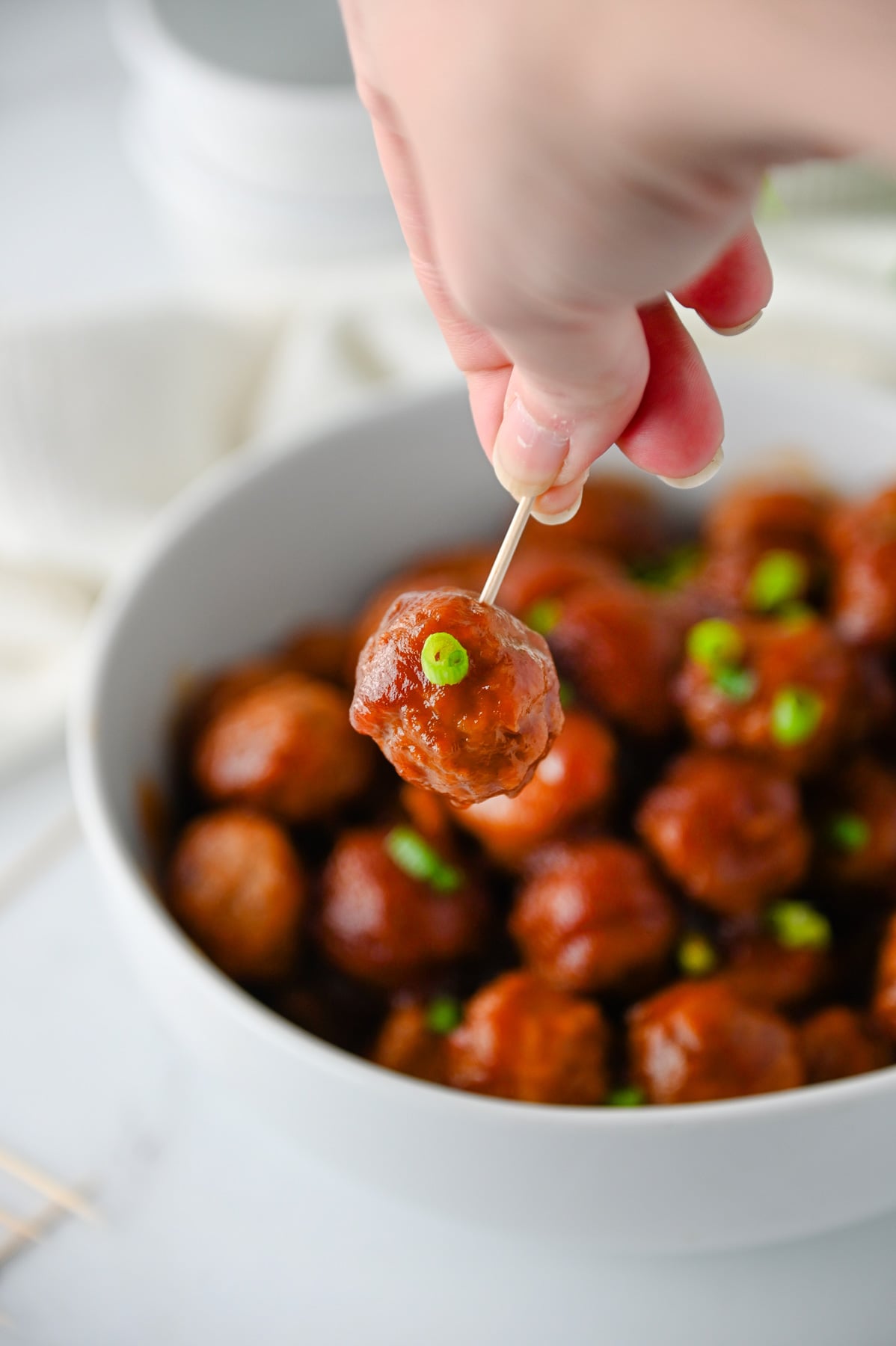 Toothpick raising meatball over bowl.