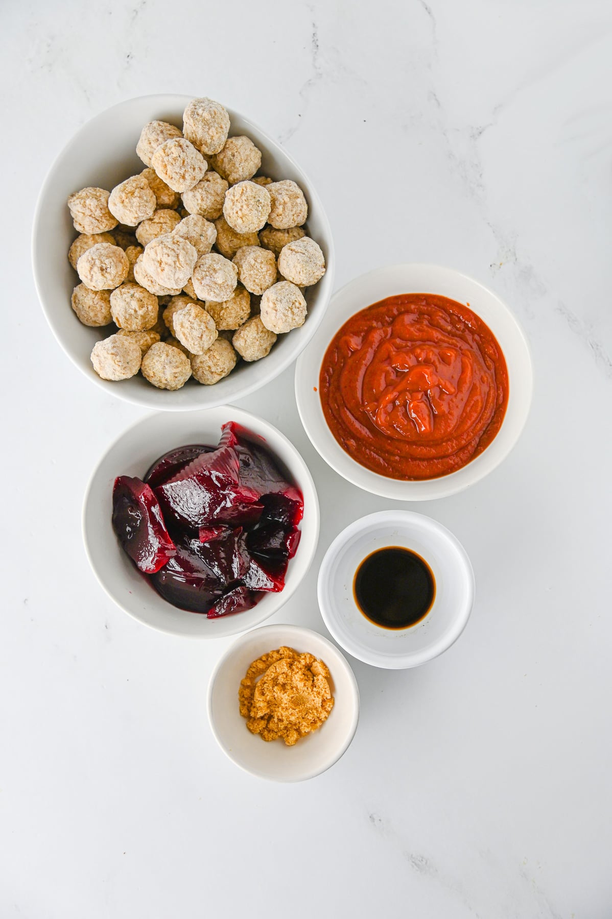 Ingredients for cranberry meatballs in small bowls on kitchen counter.