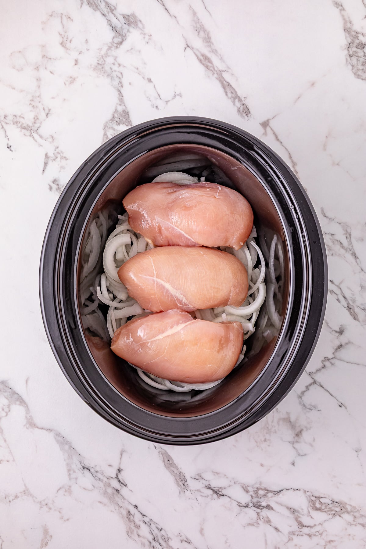 Sliced onions and chicken in bottom of crockpot.