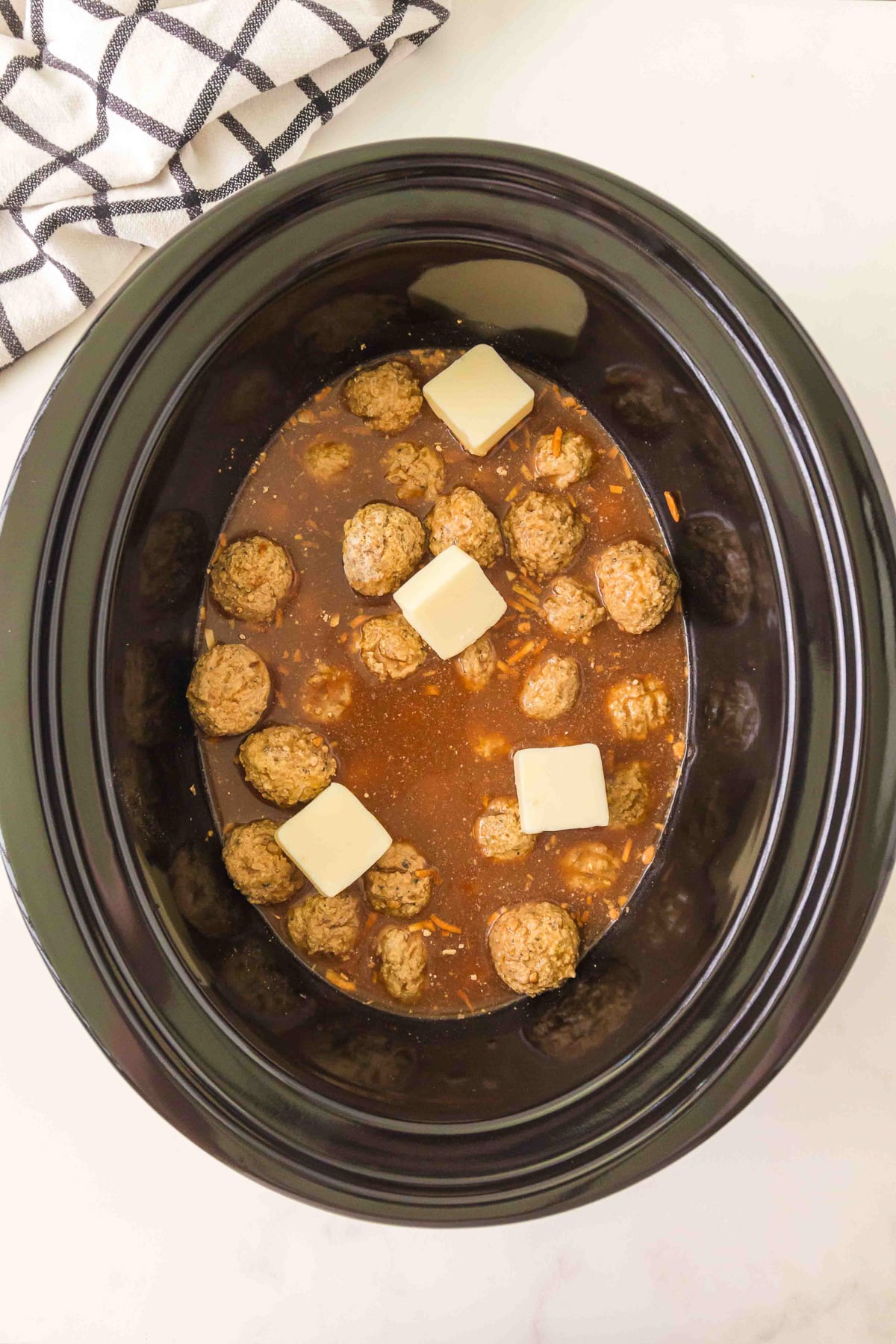 Frozen meatballs and pats of butter are added to the slow cooker.