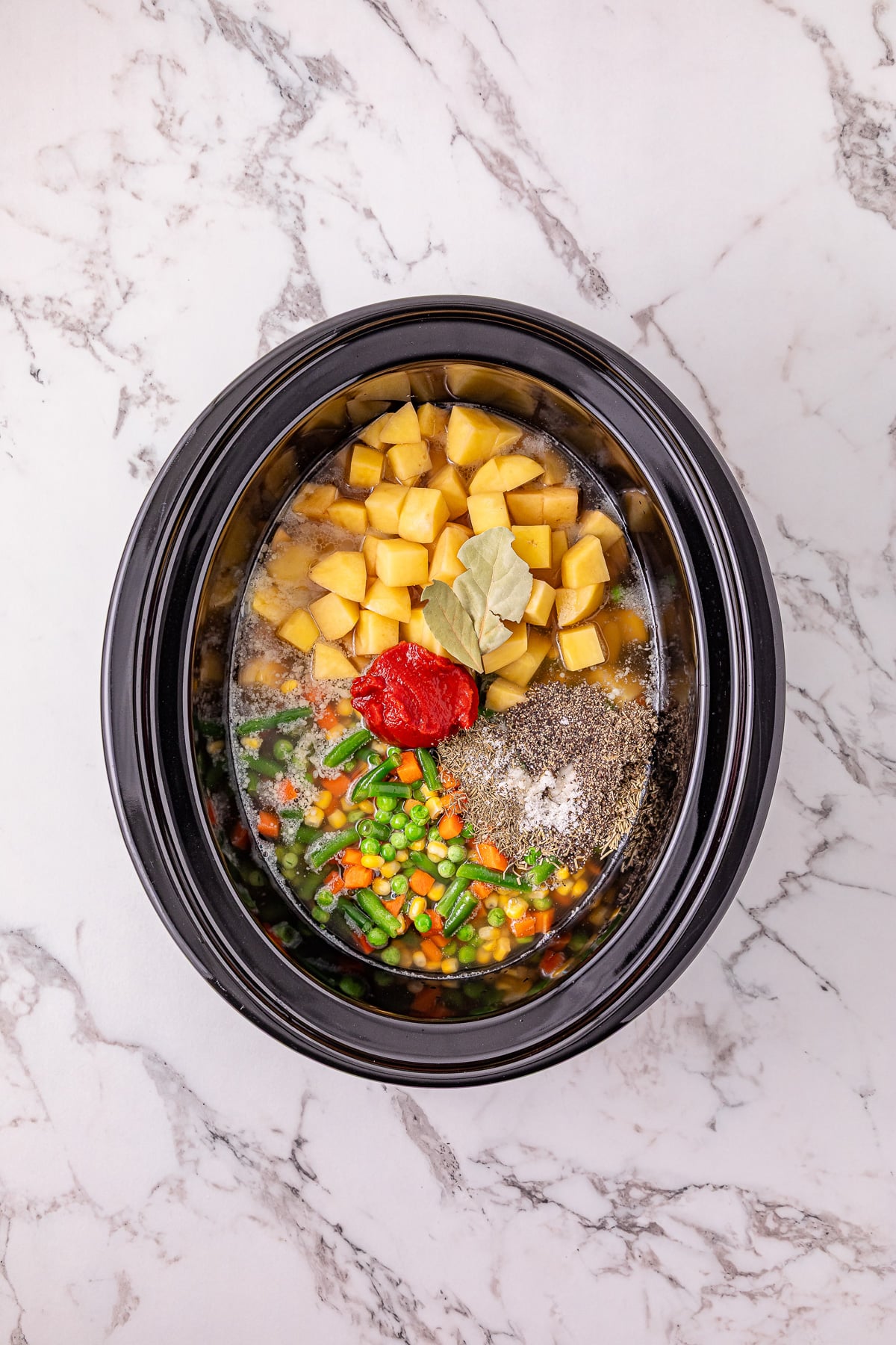 Potoates and other ingredients are added to the slow cooker, followed by the chicken broth.