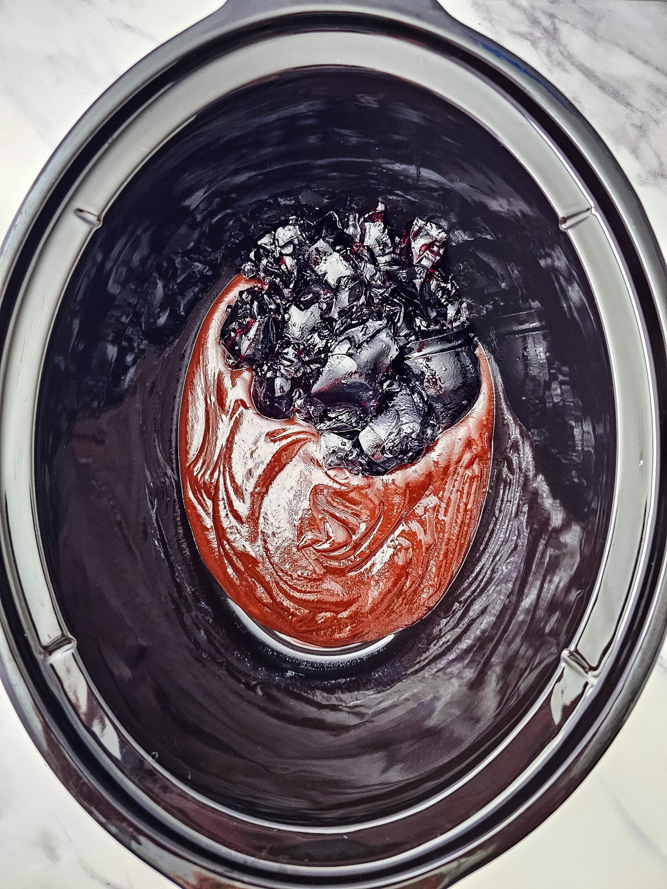 BBQ sauce and grape jelly is spread in the bottom of the slow cooker.