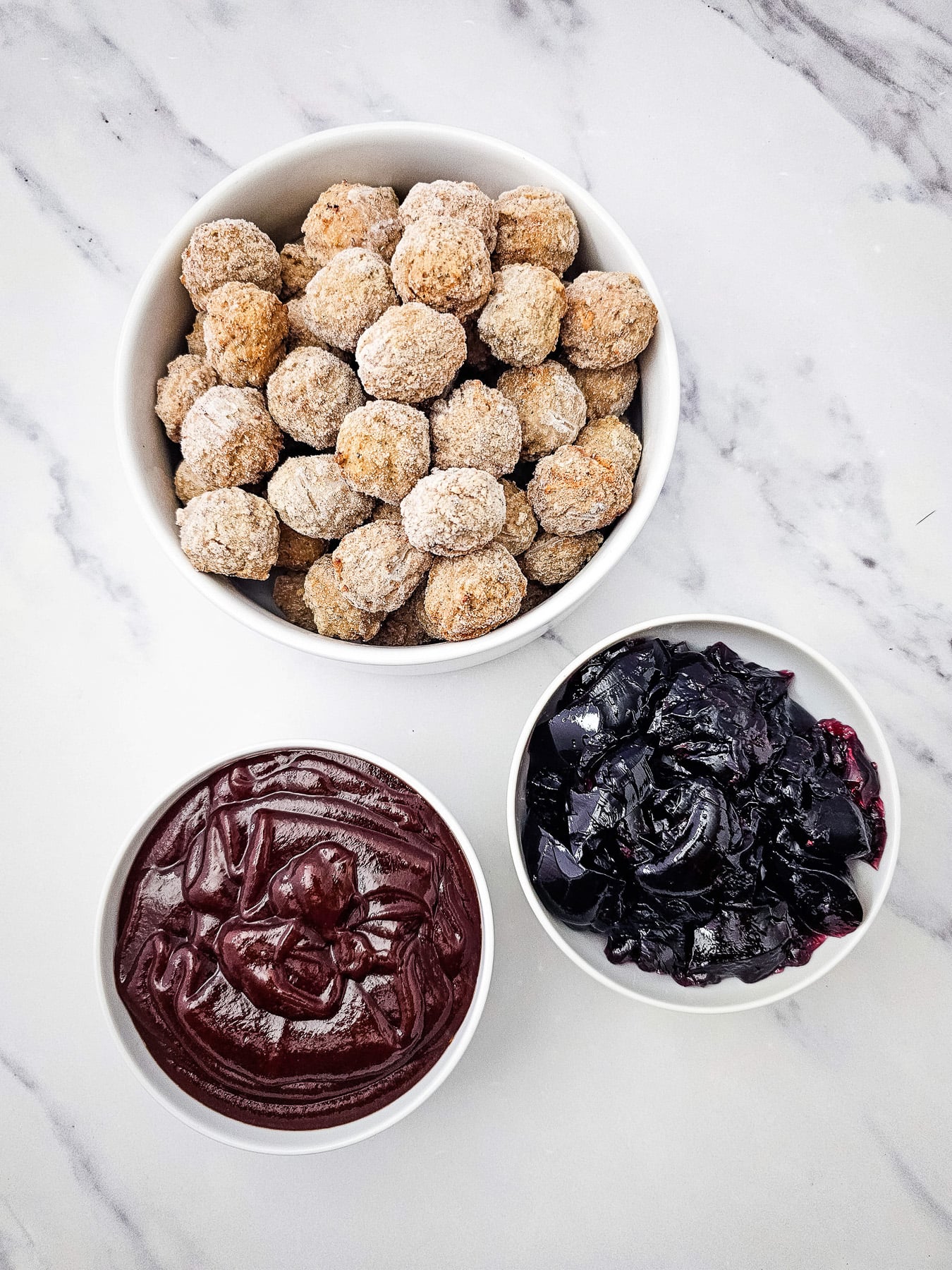 Grape jelly bbq meatballs in small bowls on kitchen counter.